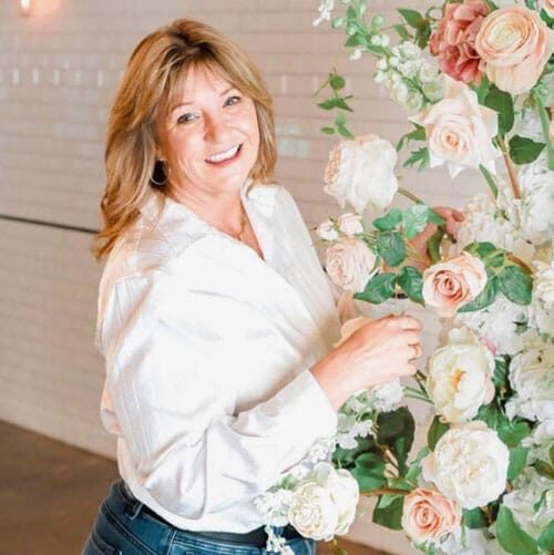 Smiling woman arranging pink and white roses in floral display at EverWild Weddings.